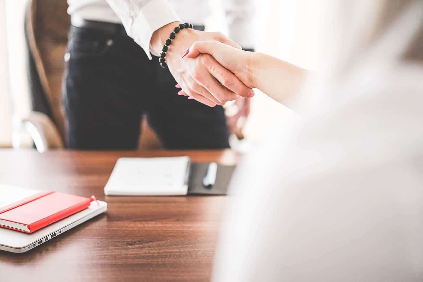 Two people shaking hands across a desk in an office