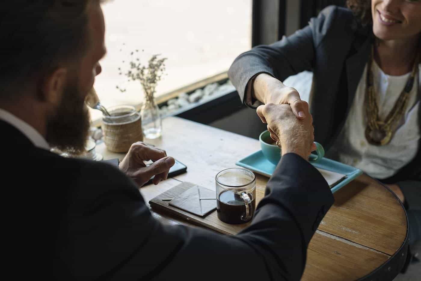 Two people shaking hands across a table in a café