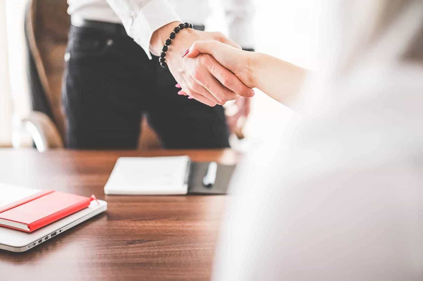 Two people shaking hands across a desk in an office