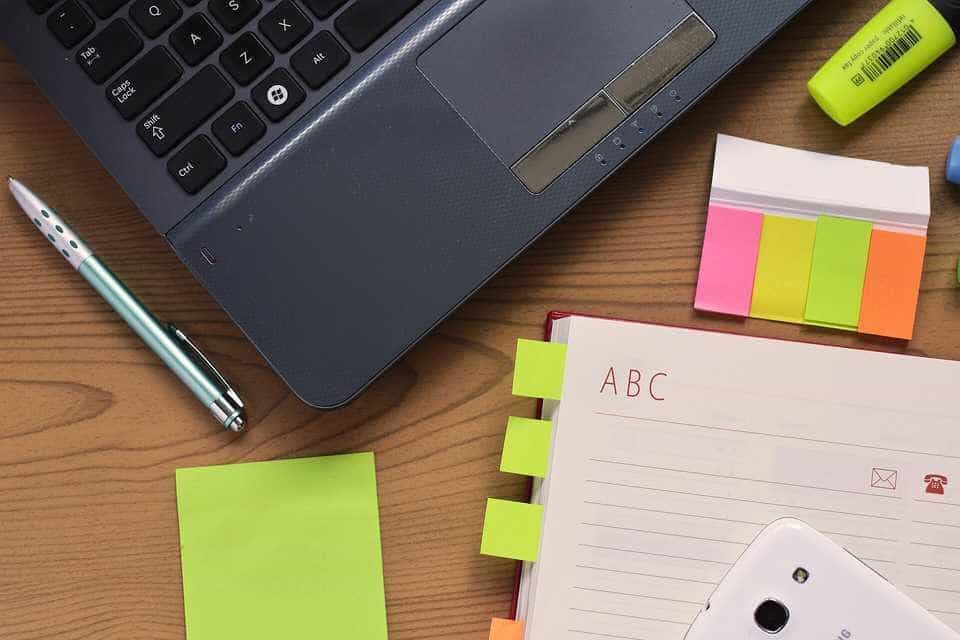 A laptop, notebook, pen and sticky notes on a wooden desk