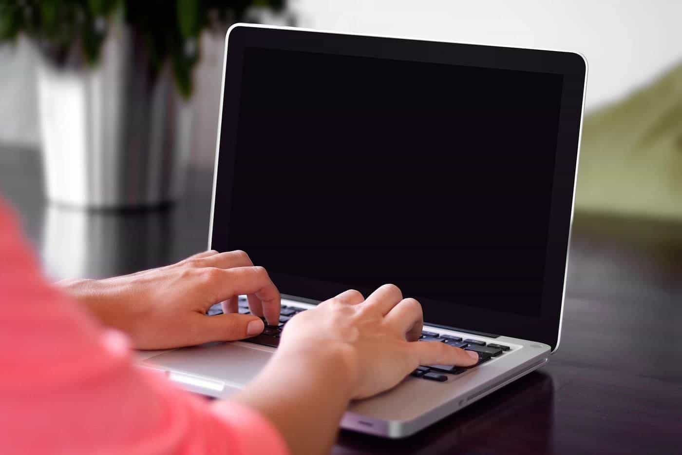 Hands typing on a laptop on a dark desk next to a pot plant